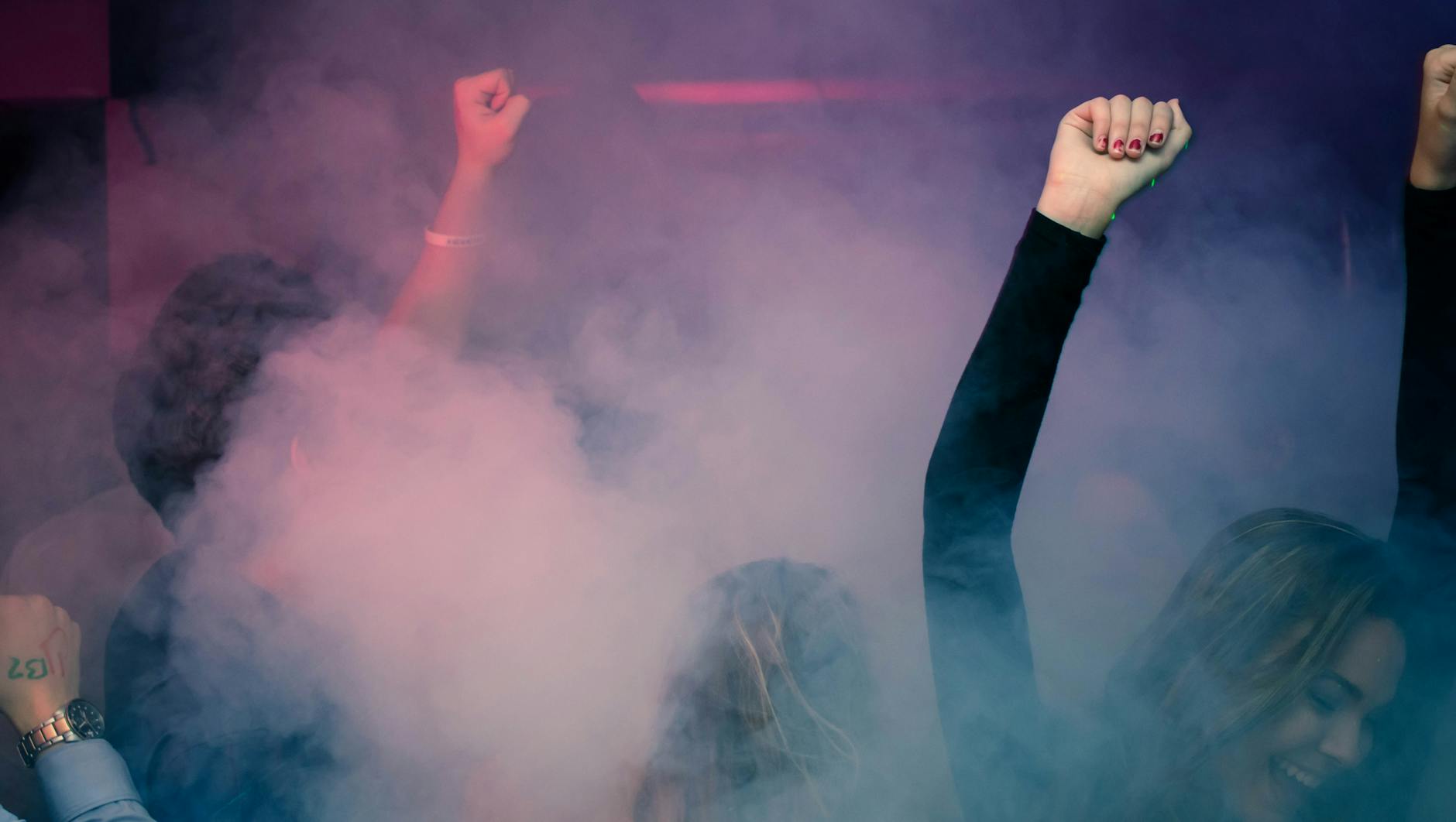 A foggy indoor scene with several women visible, with fists raised into the air.
